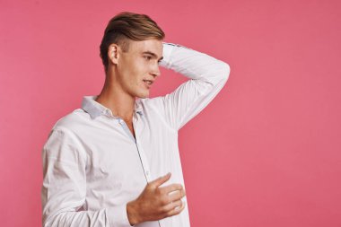 Beyaz gömlekli genç adam pembe arka planda poz veriyor.