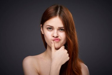 Güzel, kızıl saçlı, çıplak omuzlu, siyah arka plan pozu veren bir kadın.