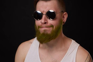 Beyaz tişörtlü, güneş gözlüklü neşeli sakallı adam poz veriyor.