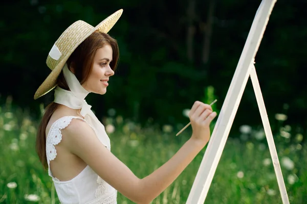 Femme en robe blanche peint un tableau sur chevalet de la nature — Photo