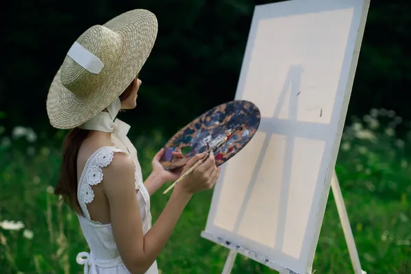 Mulher de vestido branco pinta um quadro no cavalete da natureza — Fotografia de Stock