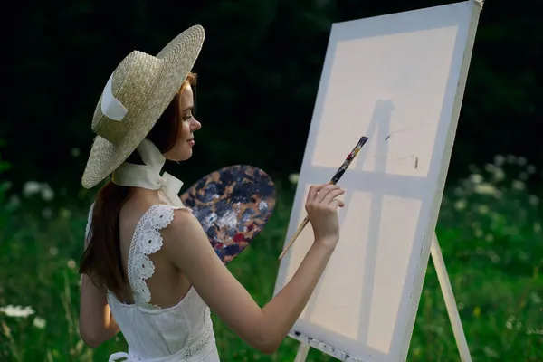Frau im weißen Kleid malt Bild auf Staffelei in der Natur — Stockfoto