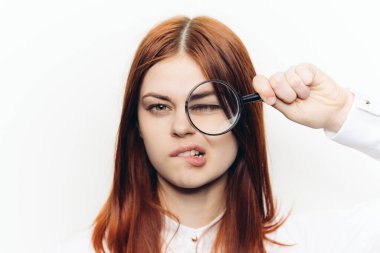 Ellerinde büyüteçle beyaz gömlekli kızıl saçlı bir kadın...