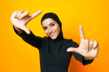 Siyah tesettürlü güzel bir kadın moda eli pozu veriyor sarı arka plan