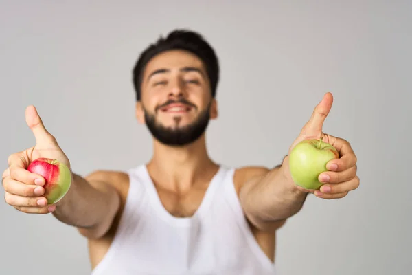 Een man in een wit t-shirt fruit voeding sterkte licht achtergrond — Stockfoto