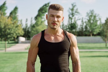 Siyah tişörtlü bir adam, doğa parkında dambıl egzersizi yapıyor.