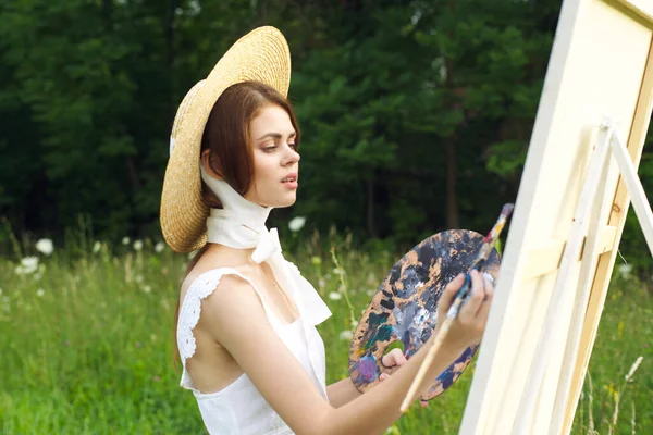 Όμορφη γυναίκα στο καπέλο καλλιτέχνης ζωγραφίζει μια εικόνα για το χρώμα της φύσης — Φωτογραφία Αρχείου