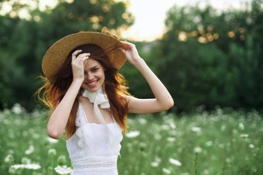 Çiçekli bir tarlada şapkalı güzel bir kadın yürüyor.