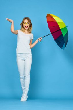 Şemsiye gökkuşağı renginde, mavi arkaplan pozu veren şık bir kadın.