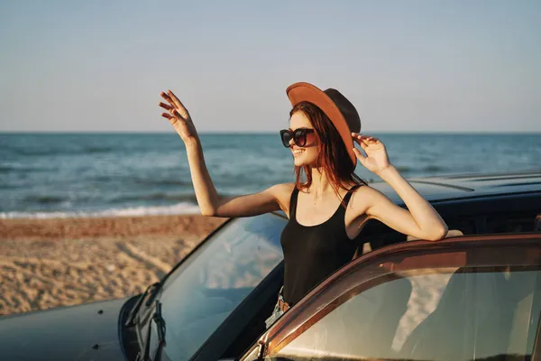 Fröhliche Frau mit Sonnenbrille und Hut auf dem Meer in der Nähe des Autos — Stockfoto