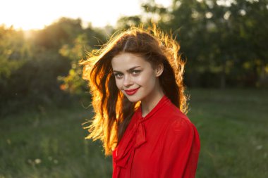 Kırmızı elbiseli kadın doğa güneşi pozu veriyor.