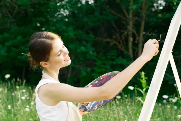 Woman artist outdoors with palette of paints paints a picture — Stock Photo, Image
