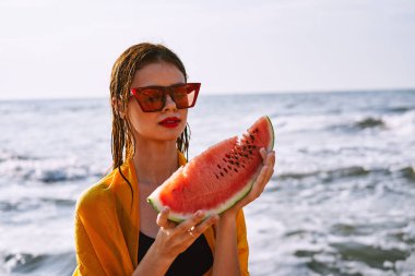 Okyanus kıyısındaki sahilde karpuz yiyen bir kadın.