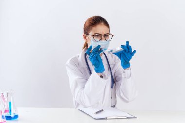 Bayan doktor mavi eldiven ve ilaç testleriyle masada oturuyor.