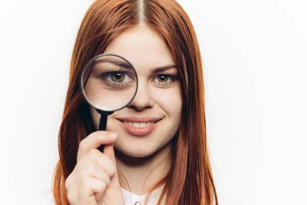 Rödhårig kvinna i vit skjorta med förstoringsglas i händerna letandes — Stockfoto