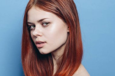 Çıplak omuzlu çekici bir kadın. Kızıl, yakın plan, mavi arka plan.