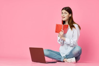 Dizüstü bilgisayar alışverişi yapan pembe arka planda oturan bir kadın.