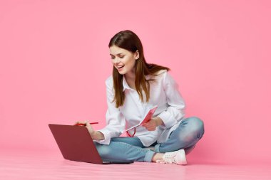 Dizüstü bilgisayar alışverişi yapan pembe arka planda oturan bir kadın.