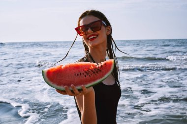 Ellerinde karpuz olan siyah mayo giymiş güzel bir kadın.