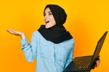 Elinde dizüstü bilgisayarla siyah tesettürlü bir kadın. Duygularını stüdyo yaşam tarzına yansıtıyor.