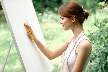 Doğada bir sanatçı kalemle sehpaya resim çizer.