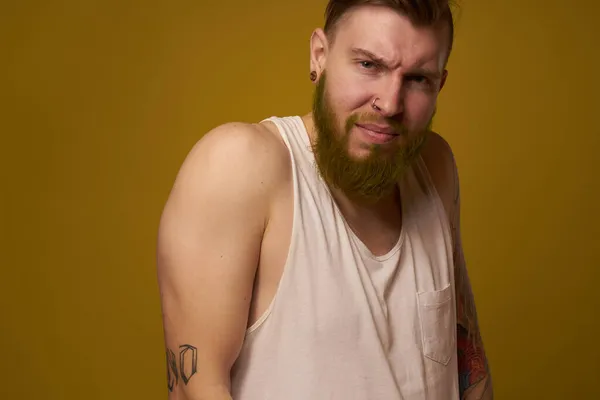A bearded man with a serious expression in a white t-shirt with tattoos on his arms — Stock Photo, Image