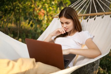 Dizüstü bilgisayarı olan kadın hamakta serbest seyahat ediyor.