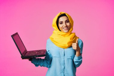 Laptop teknolojisi öğrencisi pembe geçmişli sarı tesettürlü müslüman kadın.
