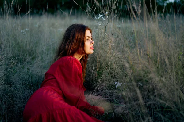 Žena na poli leží na trávě v červených šatech pózuje — Stock fotografie