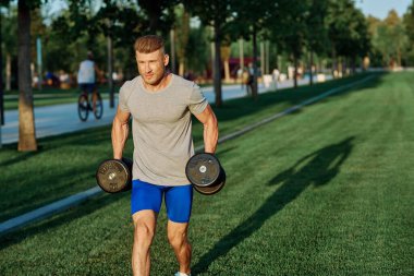 Dambılı erkek sporcu parkı CrossFit egzersizi yapıyor.