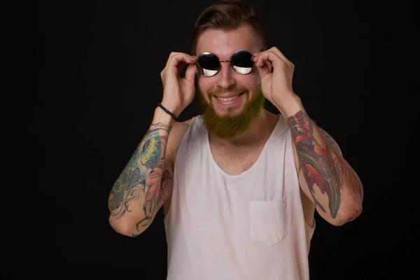 Красивий чоловік з татуюваннями на руках мода сонцезахисні окуляри темний фон — стокове фото