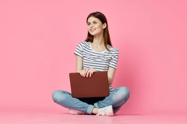 Mujer sentada en el suelo con ordenador portátil en línea compras tecnología rosa fondo — Foto de Stock
