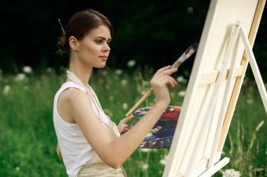 Neşeli kadın ressam açık havada yaratıcı bir resim çiziyor.