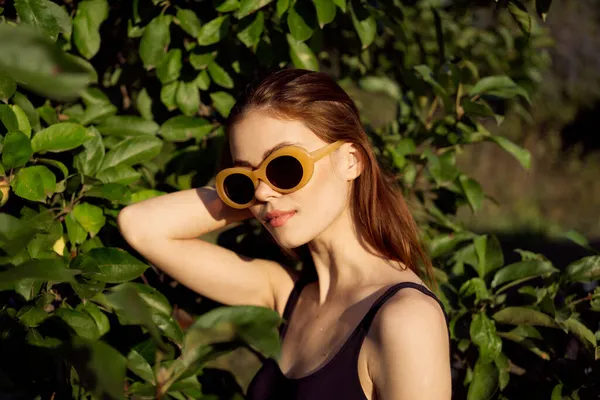 Csinos nő fekete fürdőruhában napszemüveg zöld levelek természet — Stock Fotó