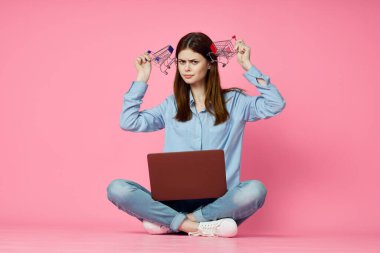 Dizüstü bilgisayarı olan bir kadın internet alışverişinde pembe arka planda oturuyor.