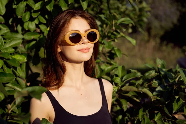 Pretty woman in black swimsuit sunglasses green leaves nature — Stock Photo, Image