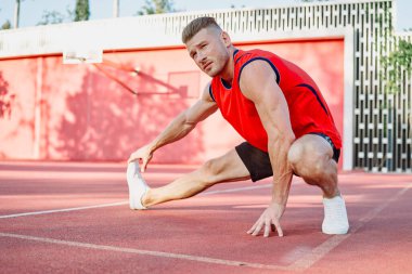 Spor salonunda spor yapan kırmızı tişörtlü bir adam egzersiz yapıyor.