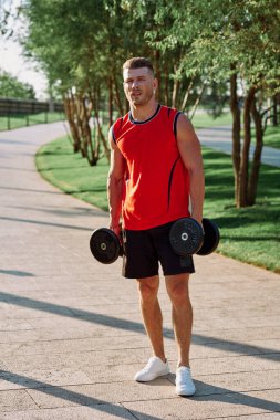 Parkın içinde elinde dambıllar olan atletik bir adam.
