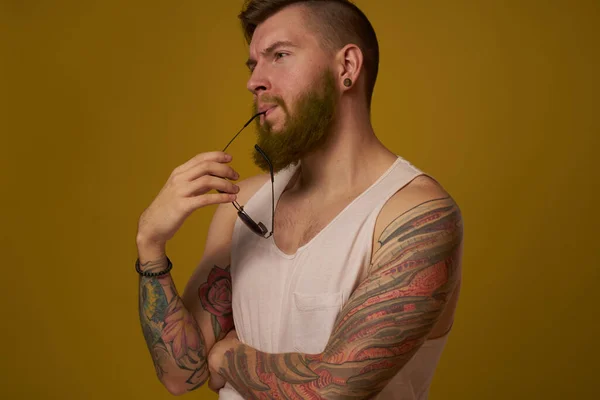 Mężczyzna w białym t-shircie tatuaże na ramionach okulary moda nowoczesny styl — Zdjęcie stockowe
