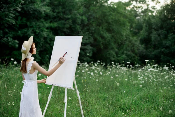 Una mujer en un vestido blanco en un campo con flores pinta un cuadro —  Fotos de Stock