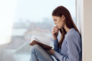 Kadın pencerenin yanında kitap okuyor, bir bardak içkiyle dinleniyor.