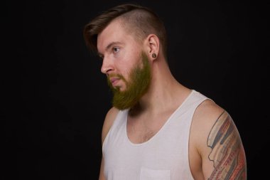 Kollarında dövmeleri olan beyaz tişörtlü şık sakallı bir adam.