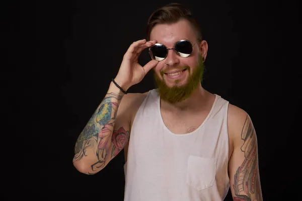 Przystojny mężczyzna z tatuażami na ramionach moda okulary przeciwsłoneczne ciemne tło — Zdjęcie stockowe
