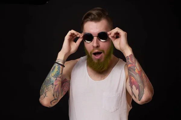 Hombre guapo con tatuajes en sus brazos gafas de sol de moda fondo oscuro — Foto de Stock
