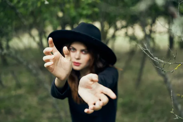 Mulher em um chapéu preto gesticulando com as mãos bruxa fantasia mágica — Fotografia de Stock