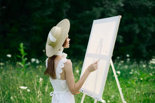 Mulher de vestido branco na natureza pinta um quadro de um hobby de paisagem — Fotografia de Stock