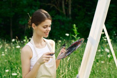 Neşeli kadın bir palet doğa resmi çiziyor.