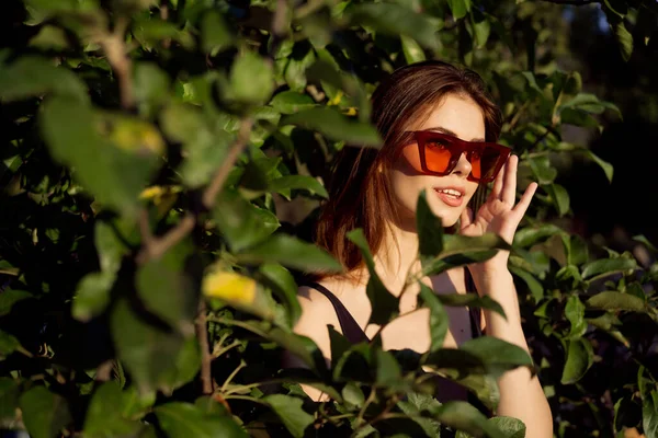 Csinos nő visel napszemüveg zöld levelek csillogás pózol nyáron — Stock Fotó