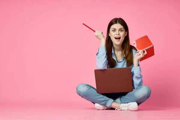 Mujer sentada en el suelo con ordenador portátil compras entretenimiento rosa fondo — Foto de Stock