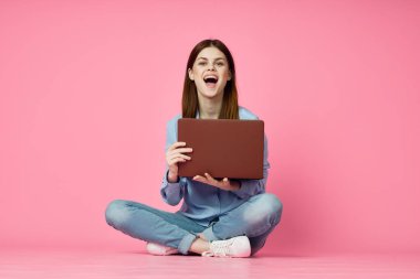 Dizüstü bilgisayar alışverişi yapan pembe arka planda oturan bir kadın.